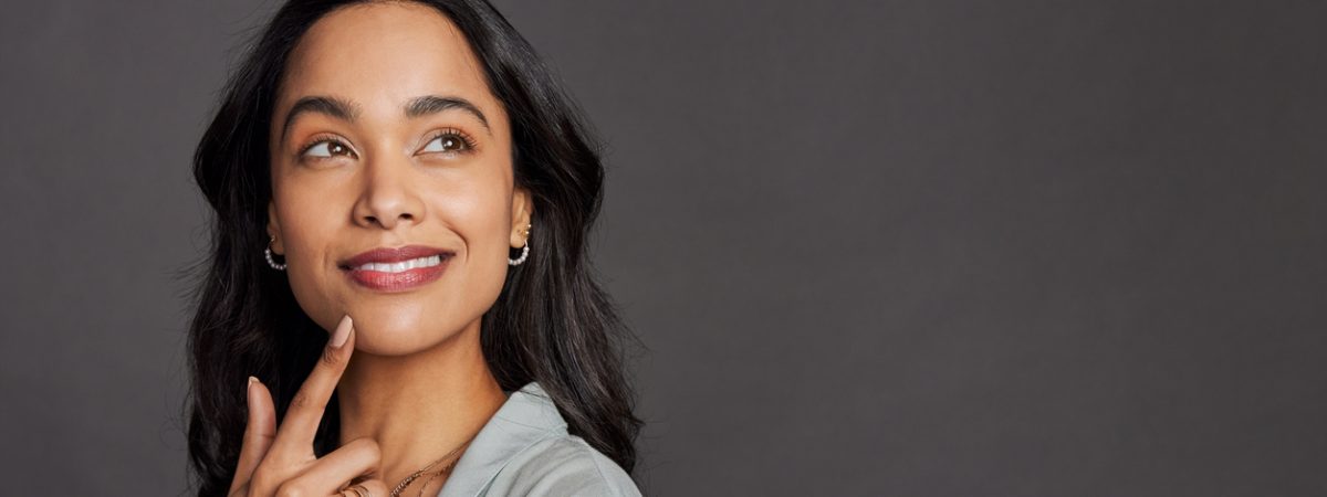 A woman smiles as she considers the value of her teeth over the significant negative costs of bargain dental work.