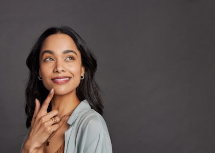 A woman smiles as she considers the value of her teeth over the significant negative costs of bargain dental work.