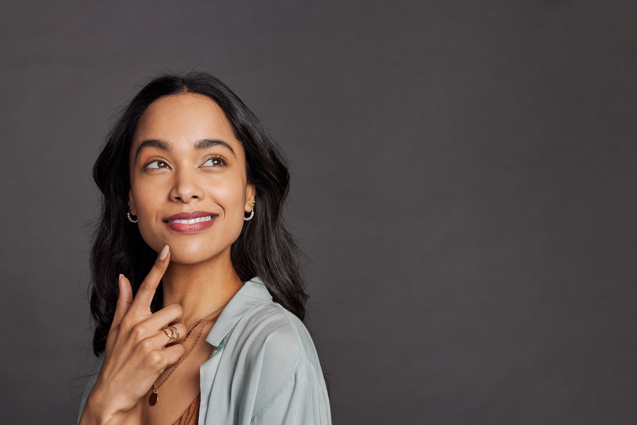 A woman smiles as she considers the value of her teeth over the significant negative costs of bargain dental work.