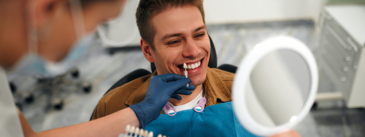 A man smiles as he holds a mirror and tries out options for porcelain veneers with his veneers dentist.