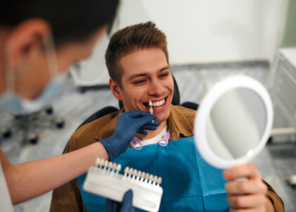 A man smiles as he holds a mirror and tries out options for porcelain veneers with his veneers dentist.