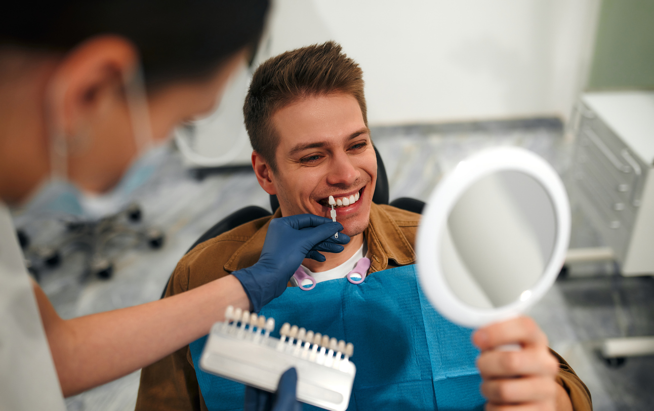 A man smiles as he holds a mirror and tries out options for porcelain veneers with his veneers dentist.