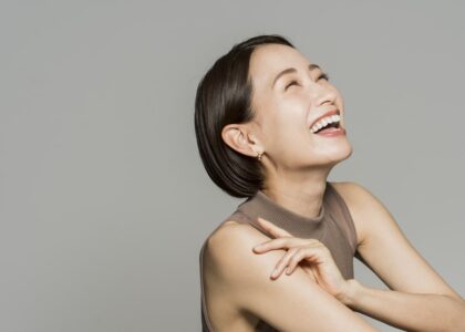 A woman with short, brunette hair smiles with confidence after receiving teeth whitening treatment, a cosmetic dentistry procedure offered by Koch Aesthetic Dentistry.