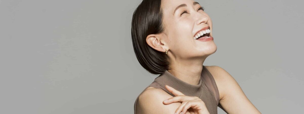 A Japanese woman with bob hair is sitting sideways and smiling.